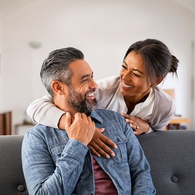 Smiling,Ethnic,Woman,Hugging,Her,Husband,On,The,Couch,From